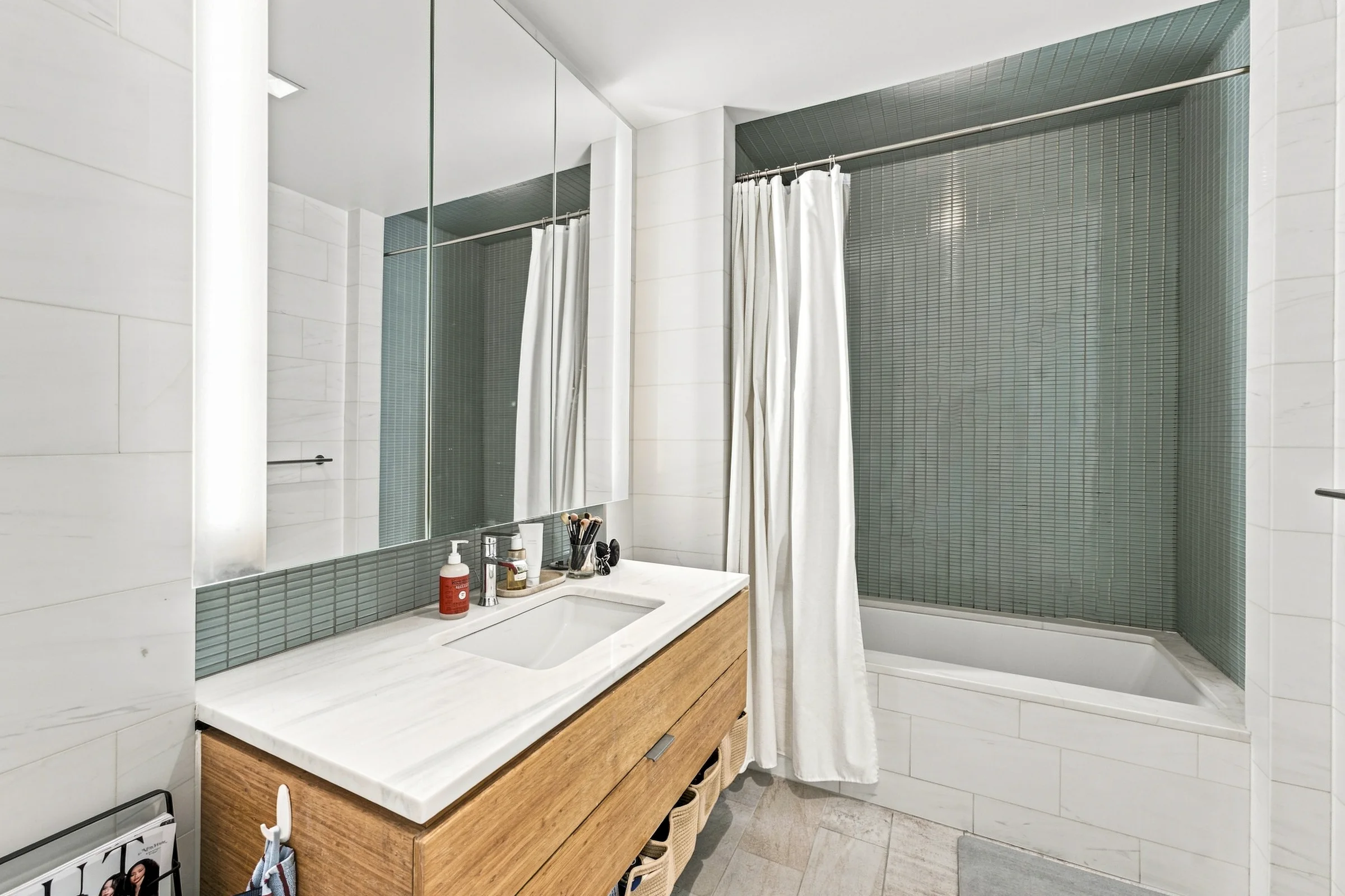 Bathroom with a wood vanity, mirrored cabinet, and green tile around the tub